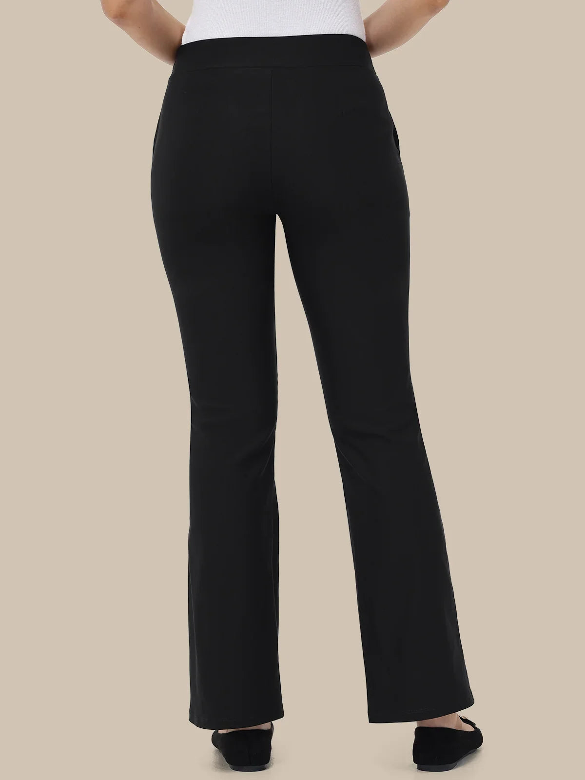 Black high-waisted flared pants shown from the back on a model, paired with a white top and black flats, against a solid beige background.