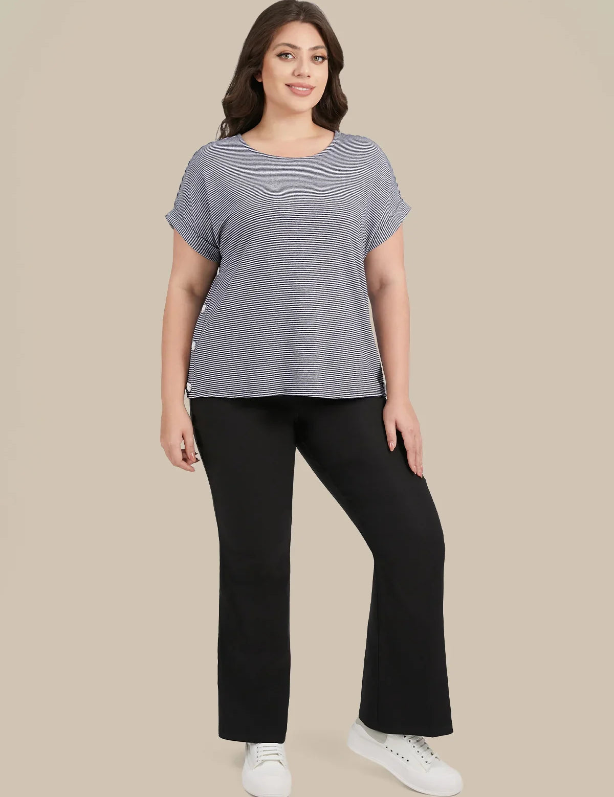 A woman modeling a heather gray short-sleeve top with ruffled edges and black pants, standing against a solid beige background.