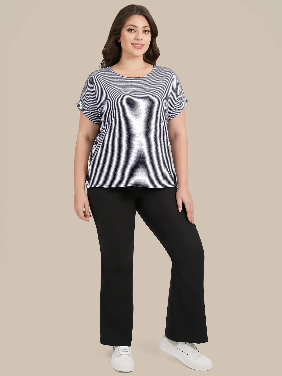 A woman modeling a heather gray short-sleeve top with ruffled edges and black pants, standing against a solid beige background.