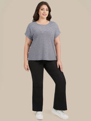 A woman modeling a heather gray short-sleeve top with ruffled edges and black pants, standing against a solid beige background.