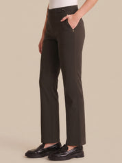 A person wearing dark olive straight-leg trousers with a white top and black loafers, shown from the waist down against a solid beige background.