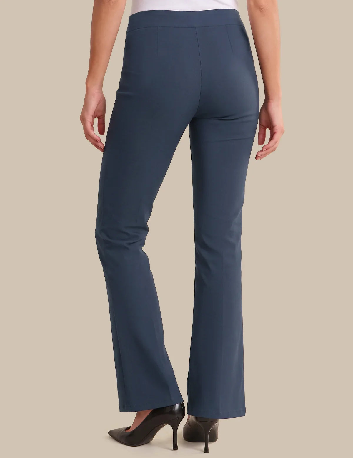 A model shown from the back wearing a pair of slate blue flare pants with black high heels, set against a solid beige background.