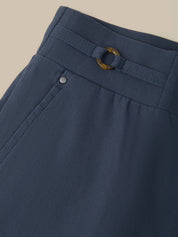 Close-up of navy blue trousers showing the waistband with a matching belt and a gold-tone ring buckle, plus a small silver button detail.