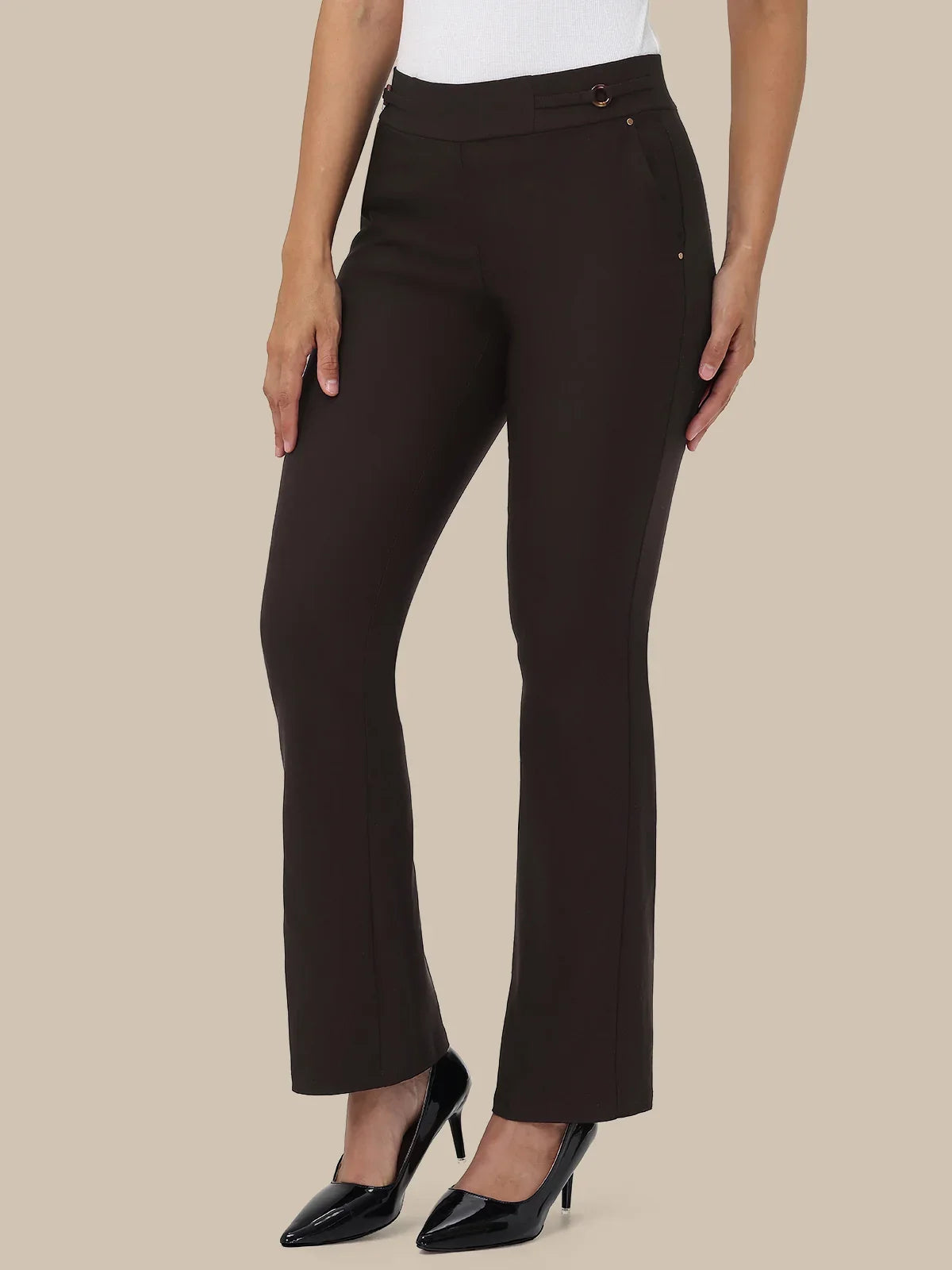 A model wearing dark brown high-waisted straight-leg trousers with a white top and black patent leather pumps, shown against a solid beige background.