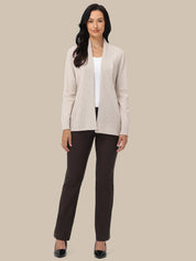 A woman modeling a light beige open-front cardigan over a white top and dark brown pants, standing against a solid beige background.