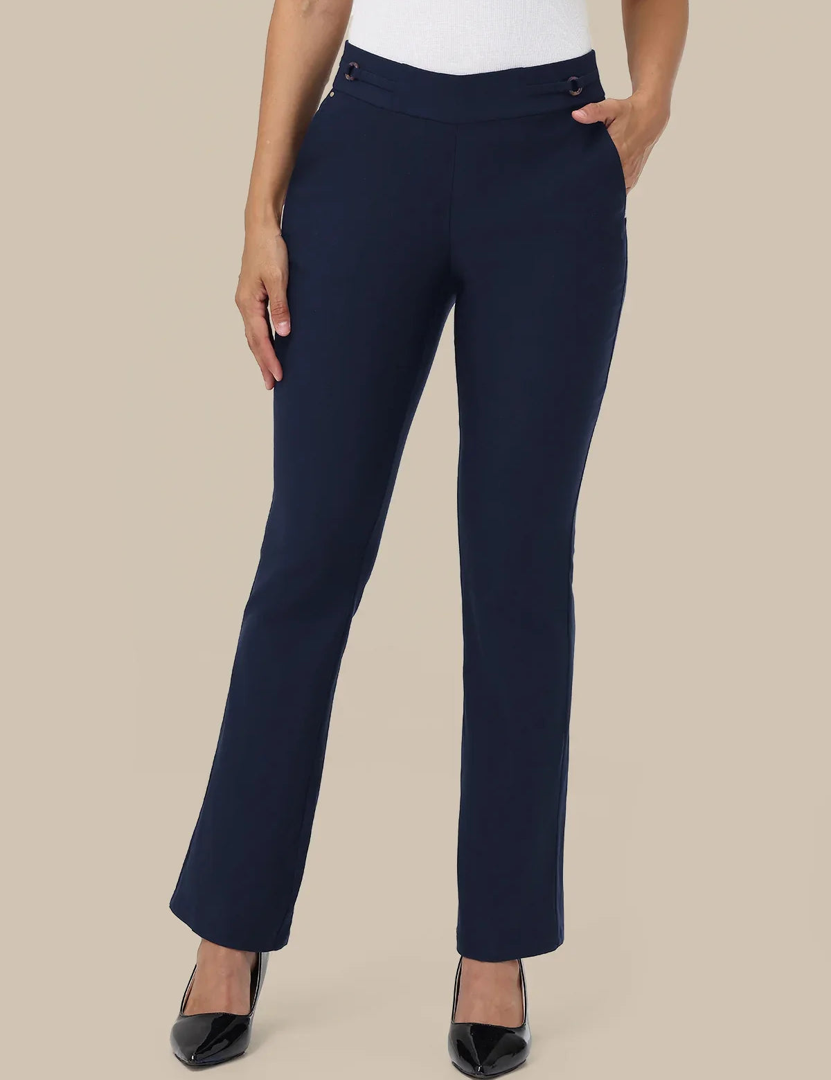 A model wearing navy blue straight-leg trousers with a white top and black pointed-toe heels, standing against a solid beige background.