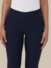 A close-up of a model wearing navy blue riding breeches with decorative brown and gold buttons on the waistband, paired with a white ribbed top against a solid beige background.
