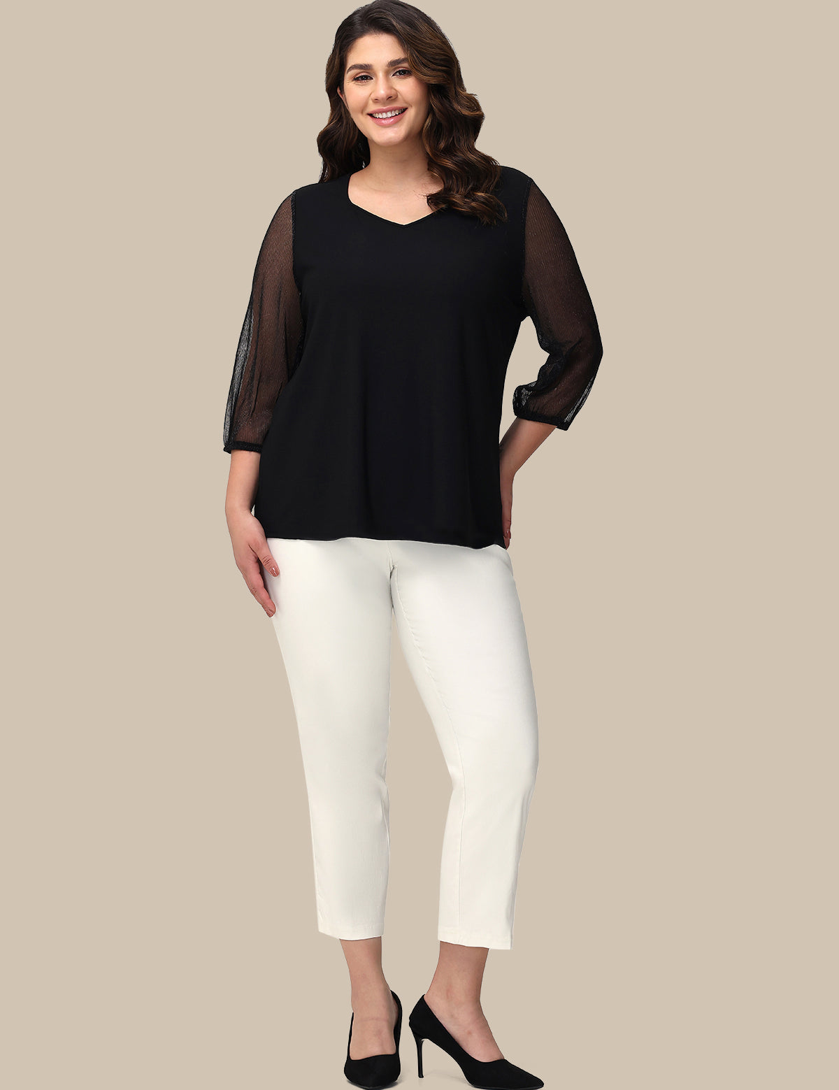Woman wearing a black top with sheer sleeves and white pants on a beige background