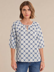 Woman wearing a blue and white patterned blouse against a beige background