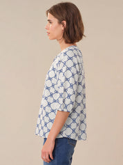 Woman wearing a blue and white patterned shirt against a beige background