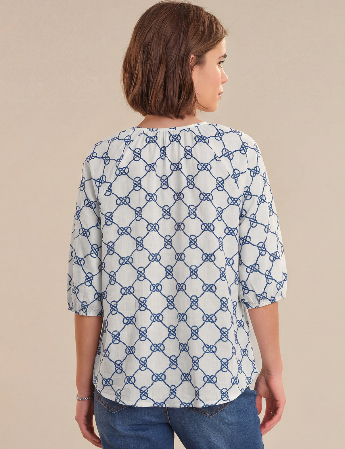 Woman wearing a white blouse with blue geometric pattern on a beige background