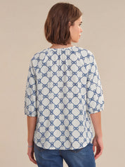 Woman wearing a white blouse with blue geometric pattern on a beige background