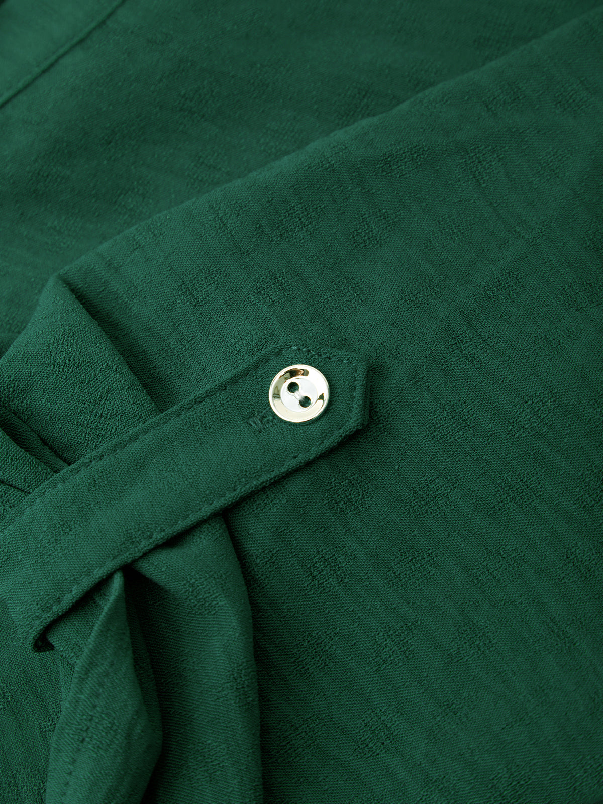 Close-up of a dark green textured fabric garment with a matching fabric tie and a small round metallic button.