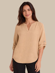A woman modeling a beige long-sleeve top with a split V-neckline and rolled sleeves, paired with black pants, against a solid beige background.