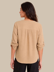 A woman shown from the back wearing a beige textured long-sleeve blouse with gathered detailing at the shoulders and rolled sleeves, paired with black pants, against a solid beige background.