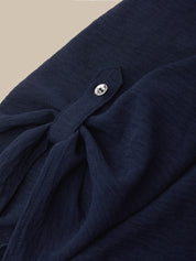 Close-up of a dark navy textured fabric garment with a small silver button detail, set against a neutral beige background.