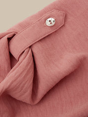 Close-up of a dusty rose pink textured fabric garment, showing a buttoned flap detail and soft folds against a warm beige background.