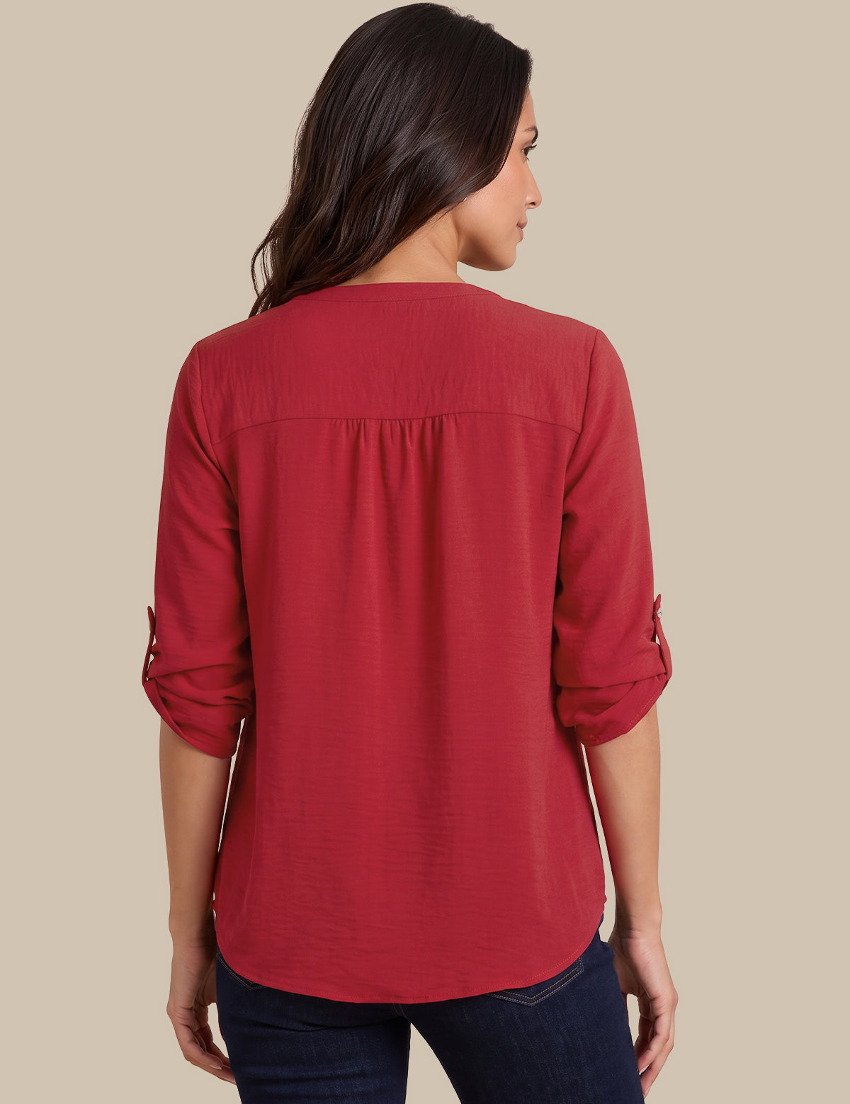 A woman shown from the back wearing a red three-quarter sleeve blouse with rolled cuffs and dark blue jeans, set against a solid beige background.