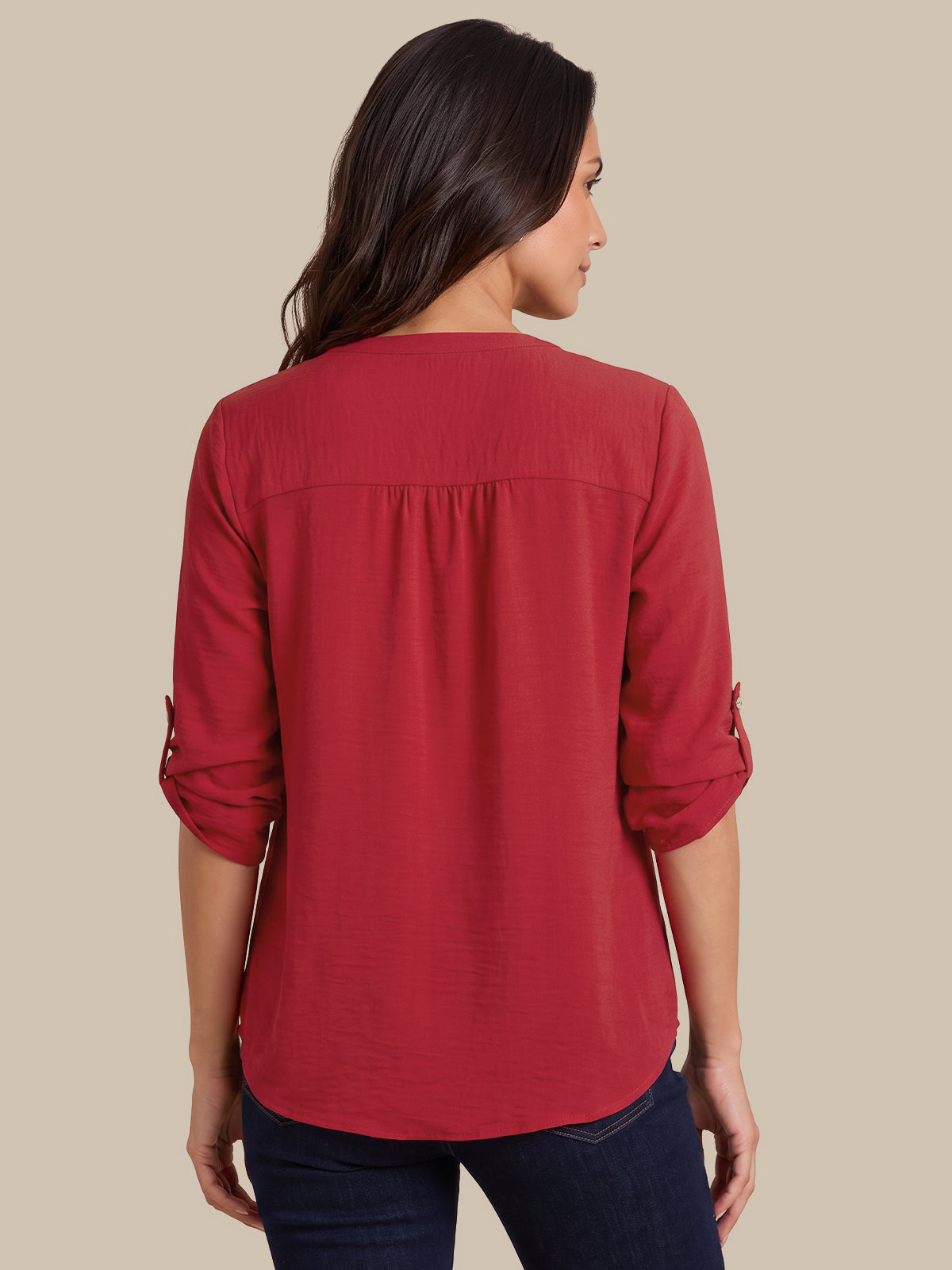 A woman shown from the back wearing a red three-quarter sleeve blouse with rolled cuffs and dark blue jeans, set against a solid beige background.