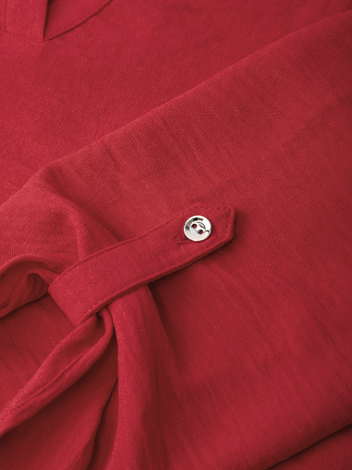 Close-up of a red textured fabric garment with a small silver button detail on a folded cuff or sleeve.