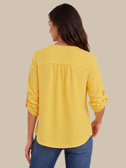 A woman shown from the back wearing a bright yellow long-sleeve blouse with rolled cuffs and blue jeans, set against a solid beige background.