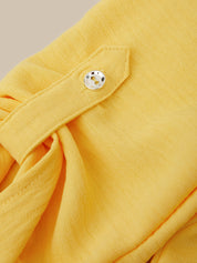 Close-up of a yellow textured fabric garment with a pointed tab and a small silver button, set against a light beige background.