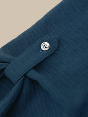Close-up of a dark teal textured fabric garment with a silver metal snap button on a beige background.