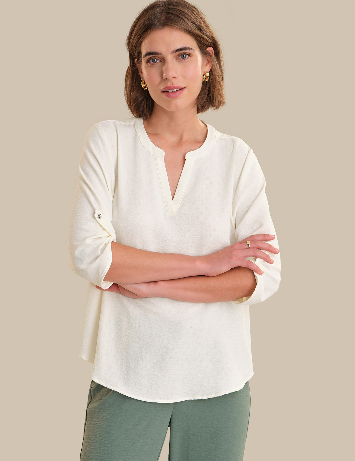 Woman wearing a white blouse with green pants against a beige background