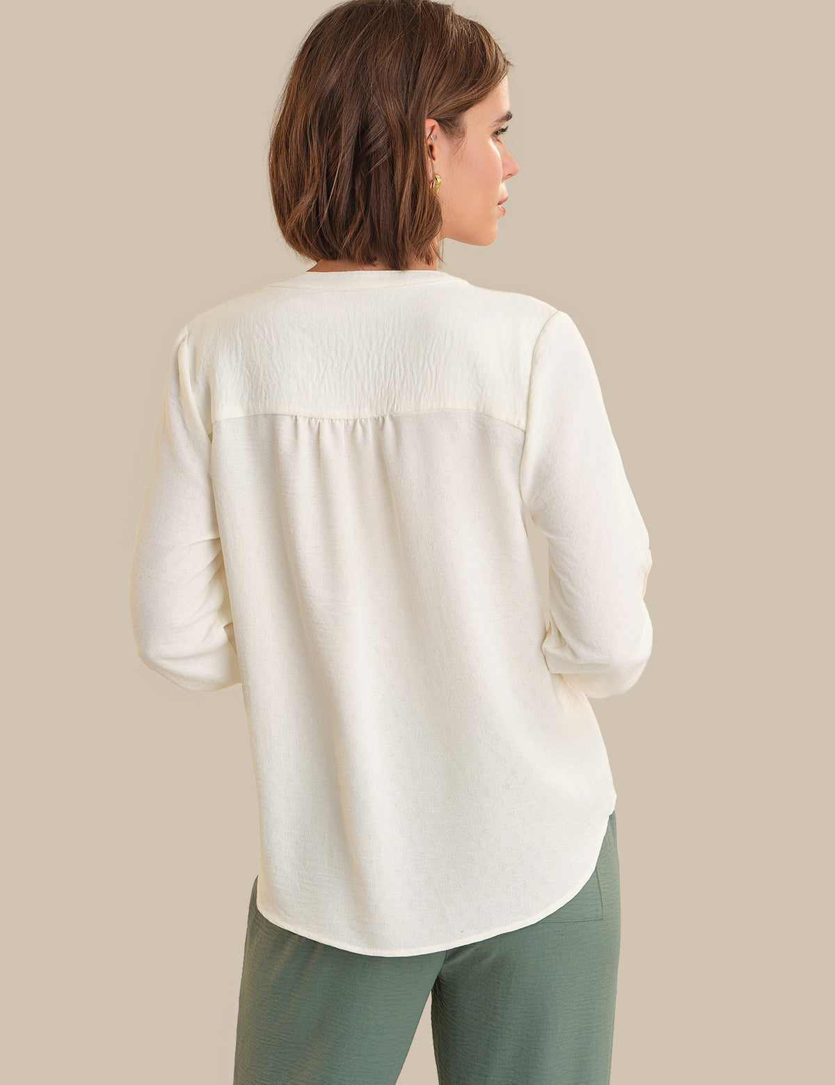 Woman wearing a white blouse and green pants against a beige background