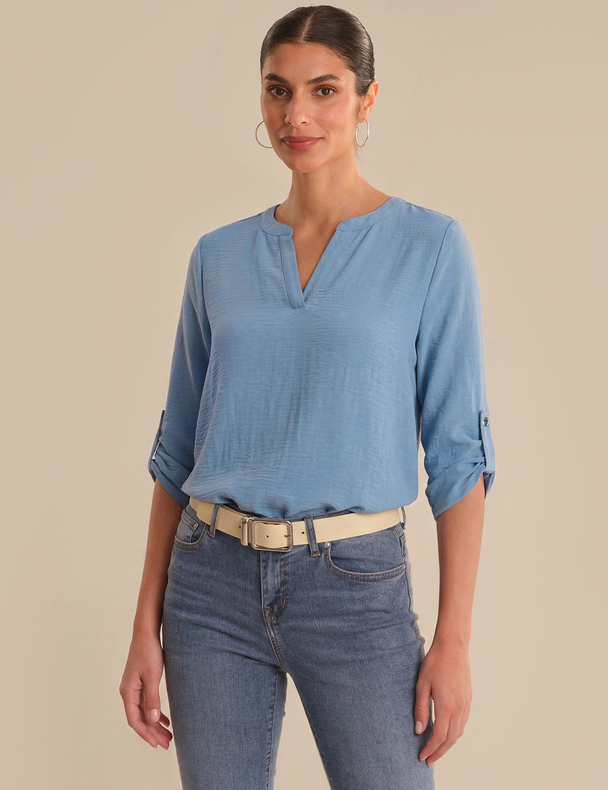 Woman wearing a blue blouse and jeans against a beige background