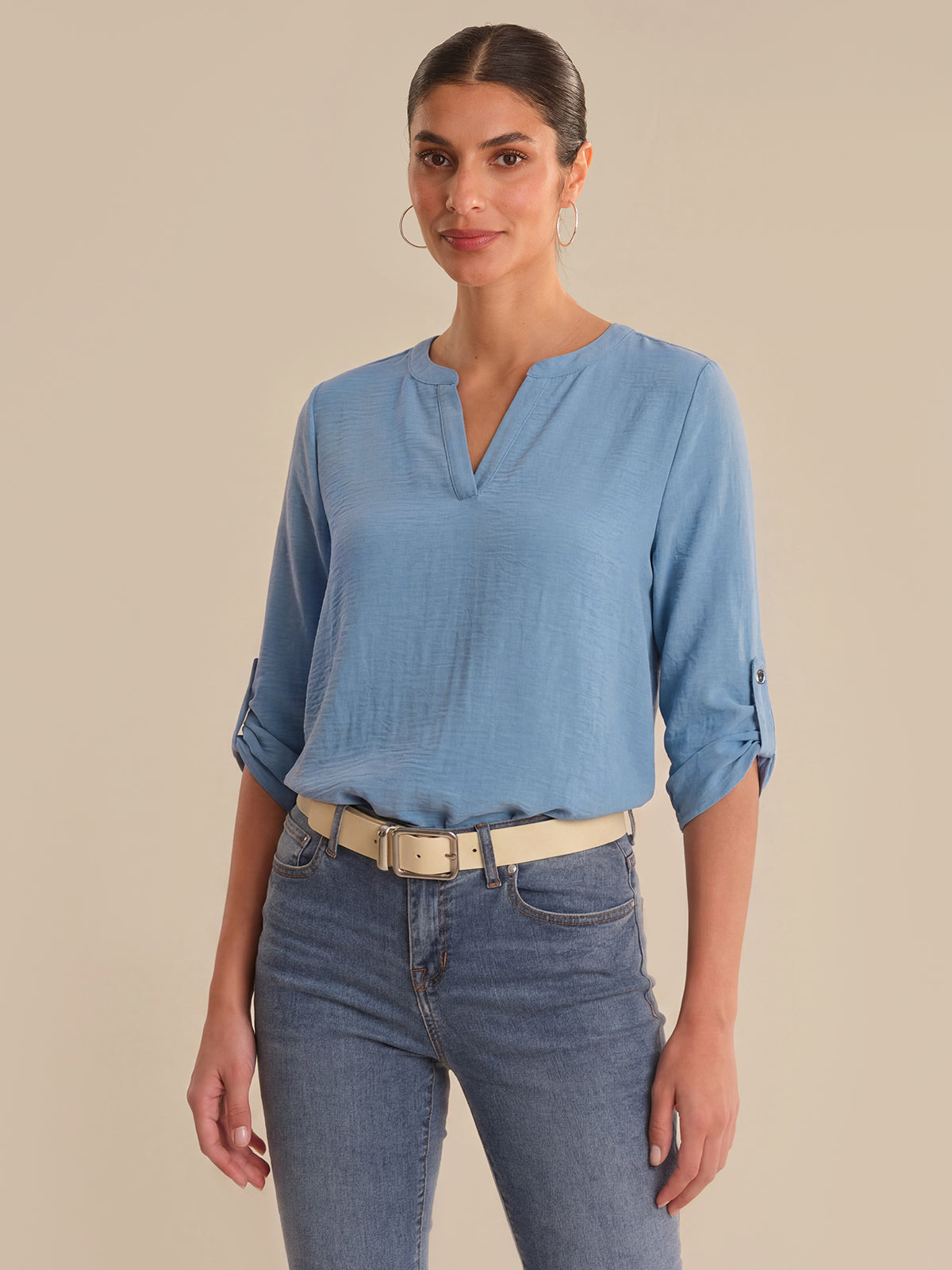 Woman wearing a blue blouse and jeans against a beige background