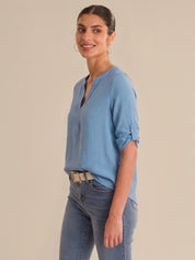 Woman wearing a blue shirt and jeans against a beige background