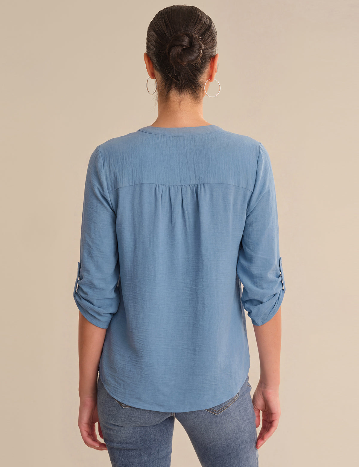 Person wearing a blue long-sleeve shirt with rolled-up sleeves on a beige background