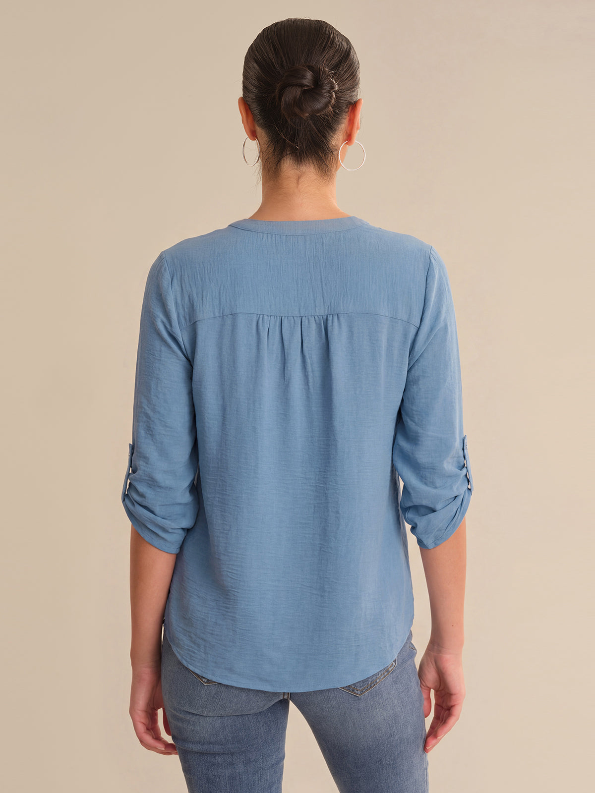 Person wearing a blue long-sleeve shirt with rolled-up sleeves on a beige background