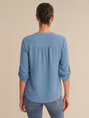 Person wearing a blue long-sleeve shirt with rolled-up sleeves on a beige background