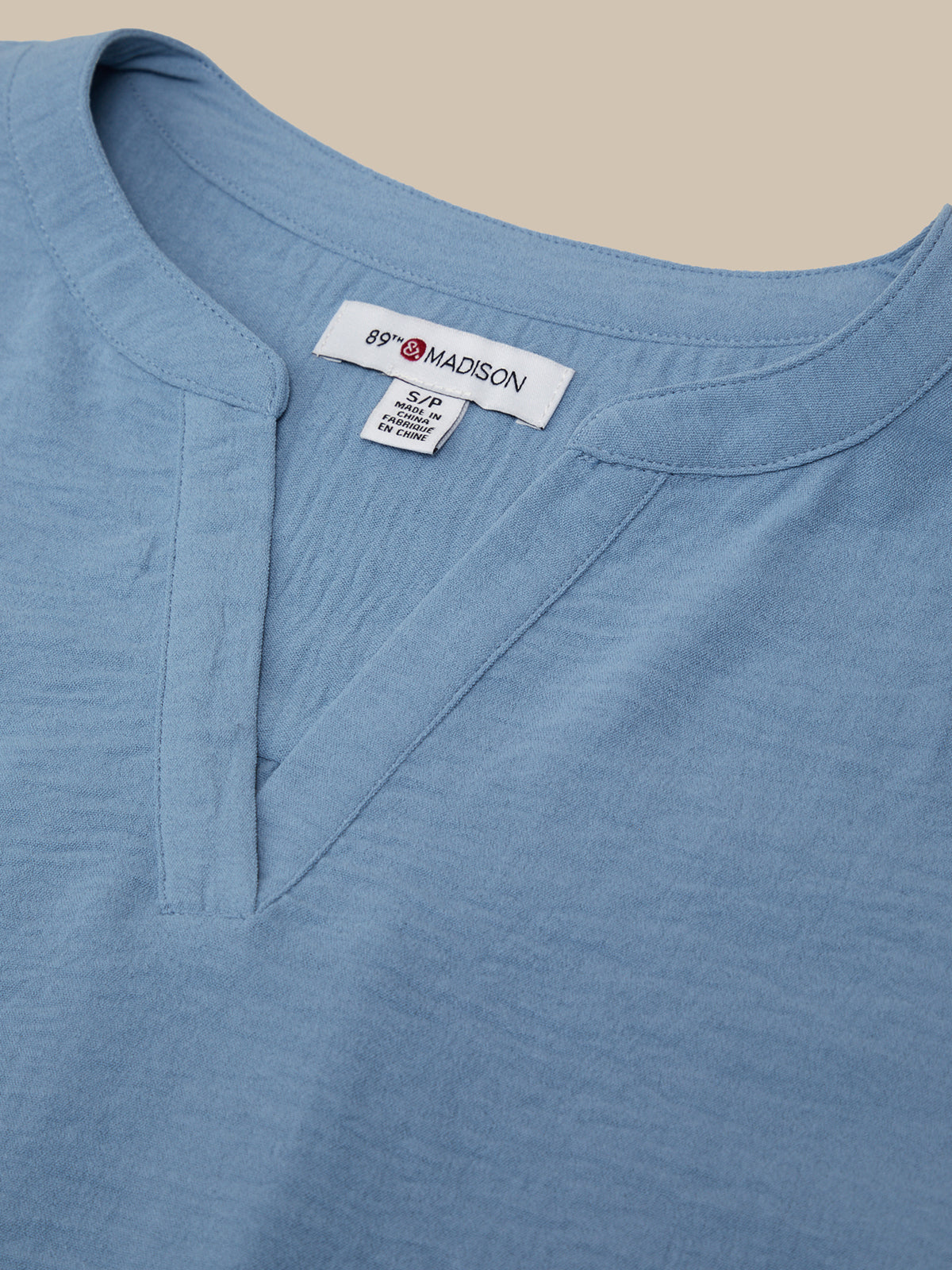 Close-up of a blue shirt with a 'Madison' label on a beige background