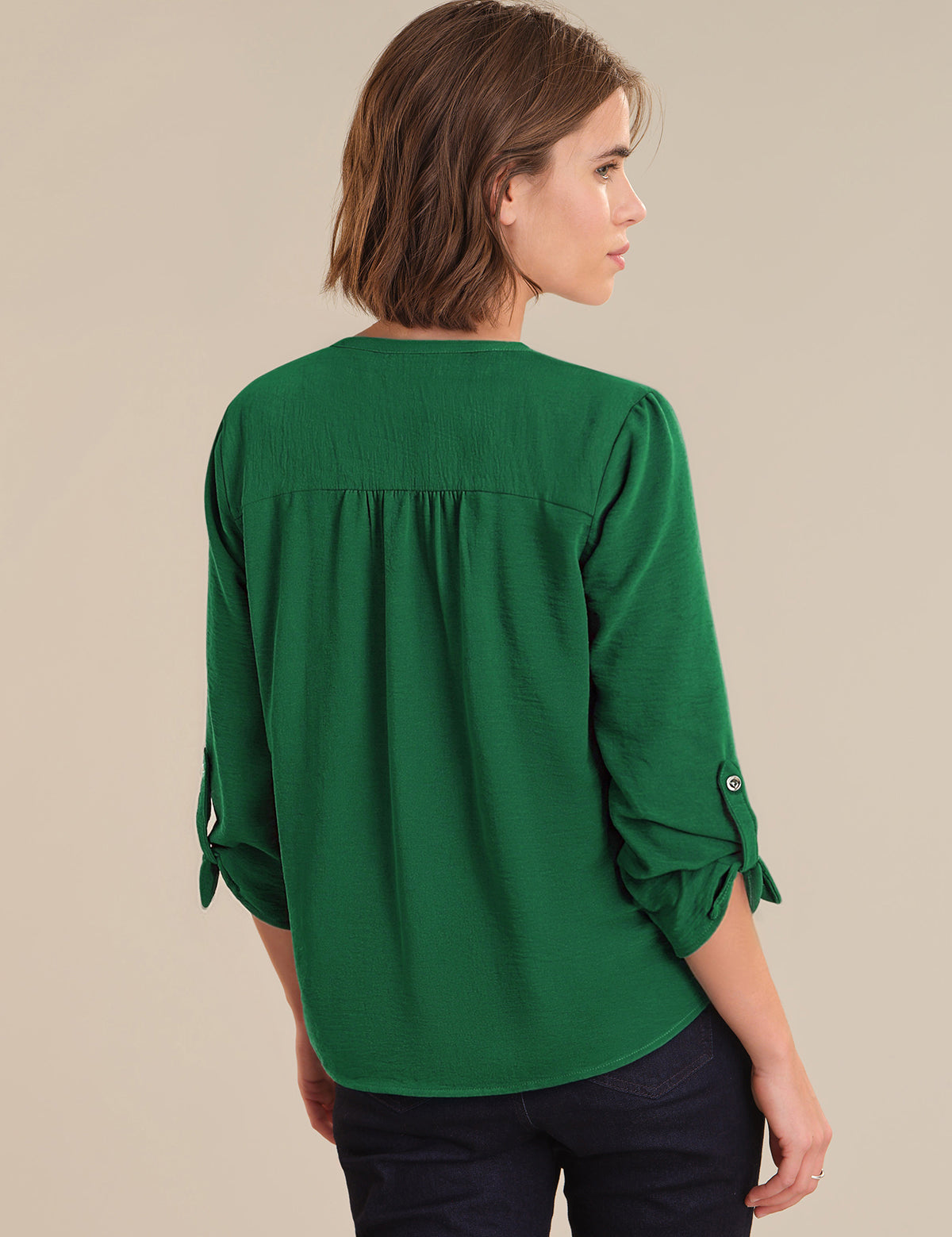 Woman wearing a green blouse with rolled-up sleeves on a beige background