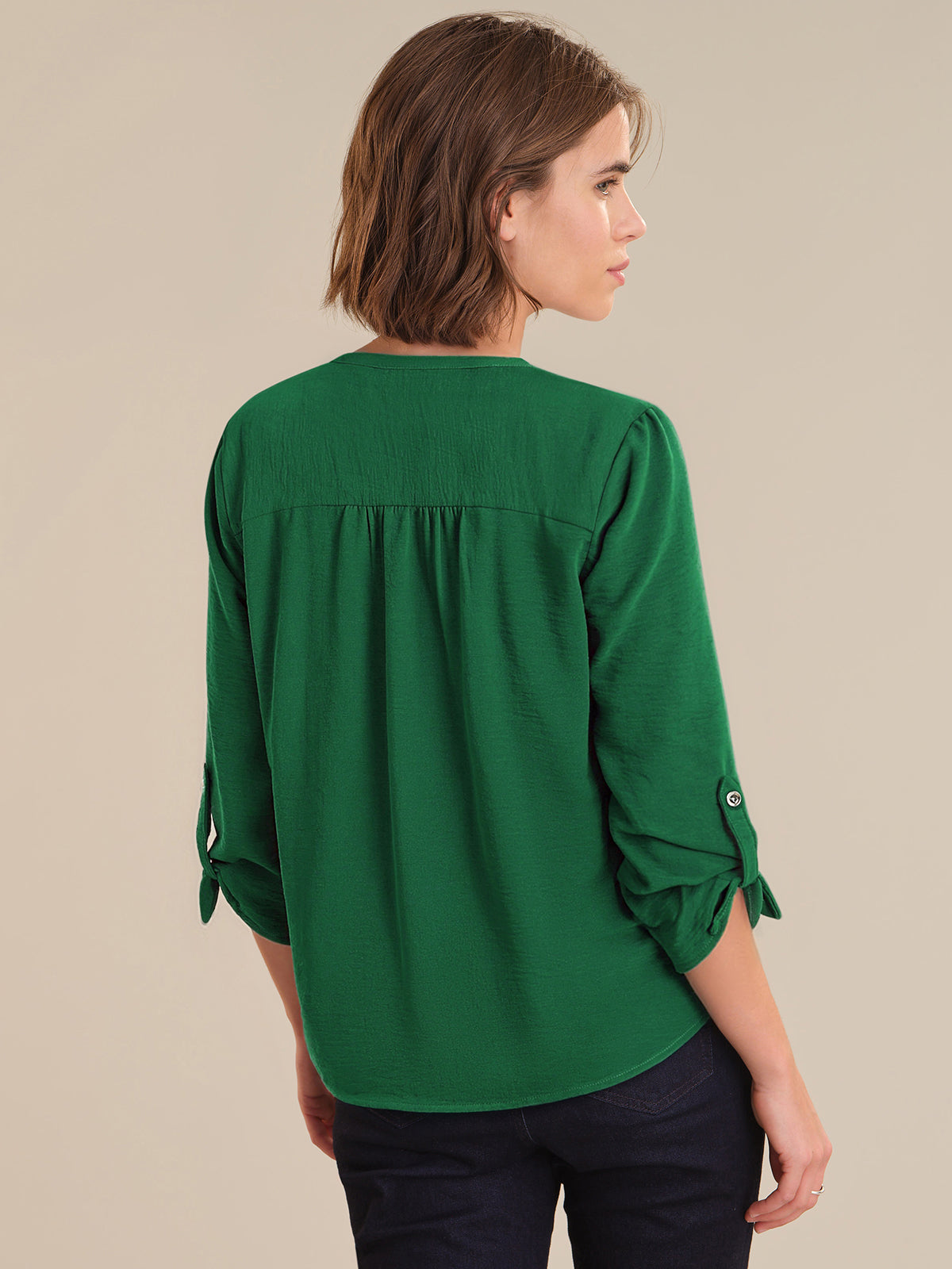 Woman wearing a green blouse with rolled-up sleeves on a beige background