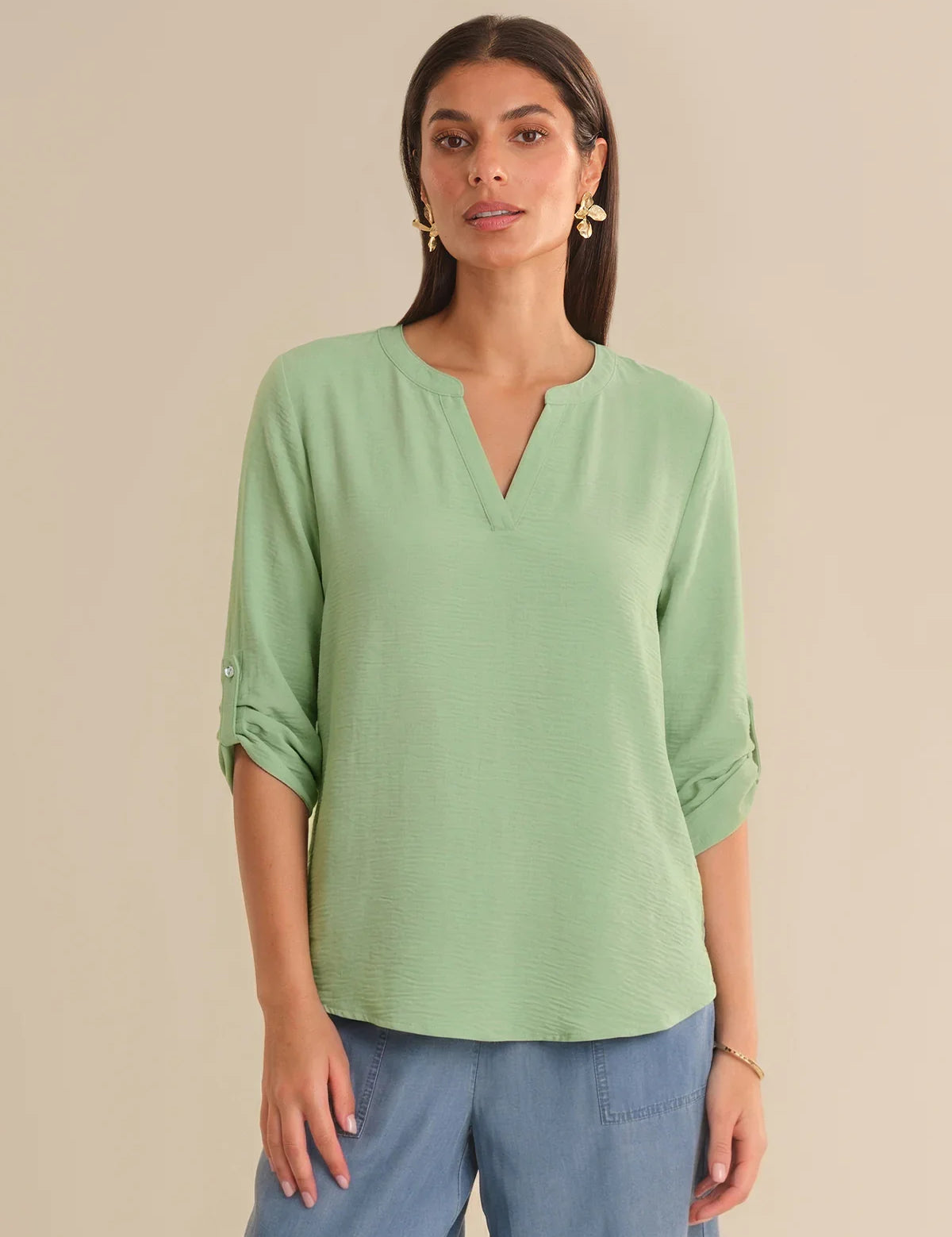 Woman wearing a light green blouse with rolled-up sleeves on a beige background