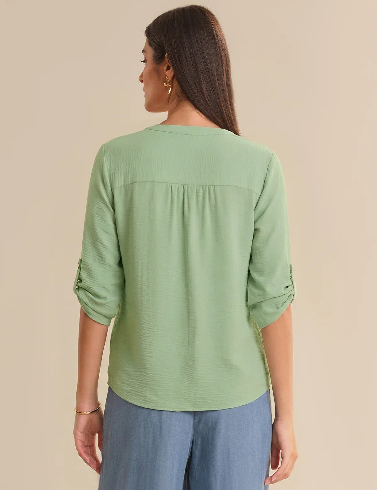 Woman wearing a green textured top with rolled-up sleeves on a beige background