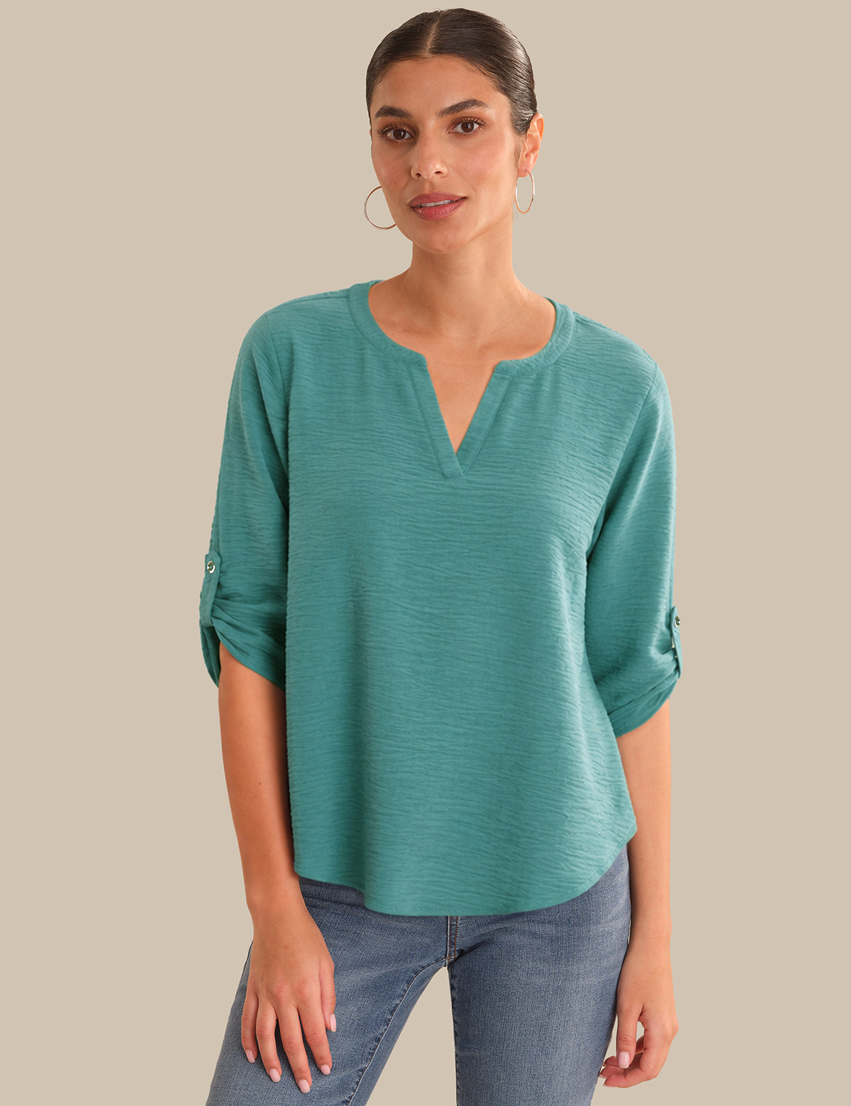 Woman wearing a teal top and jeans on a beige background