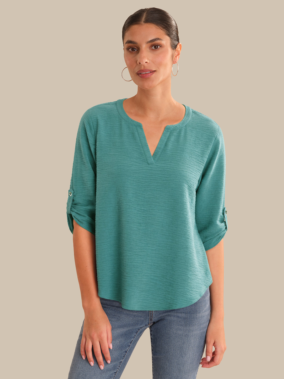 Woman wearing a teal top and jeans on a beige background