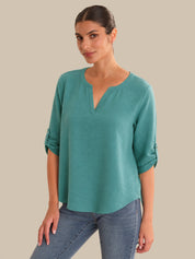 Woman wearing a teal top and jeans against a beige background