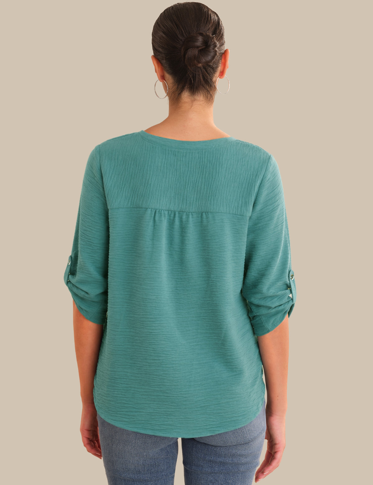 Person wearing a teal long-sleeve top on a beige background