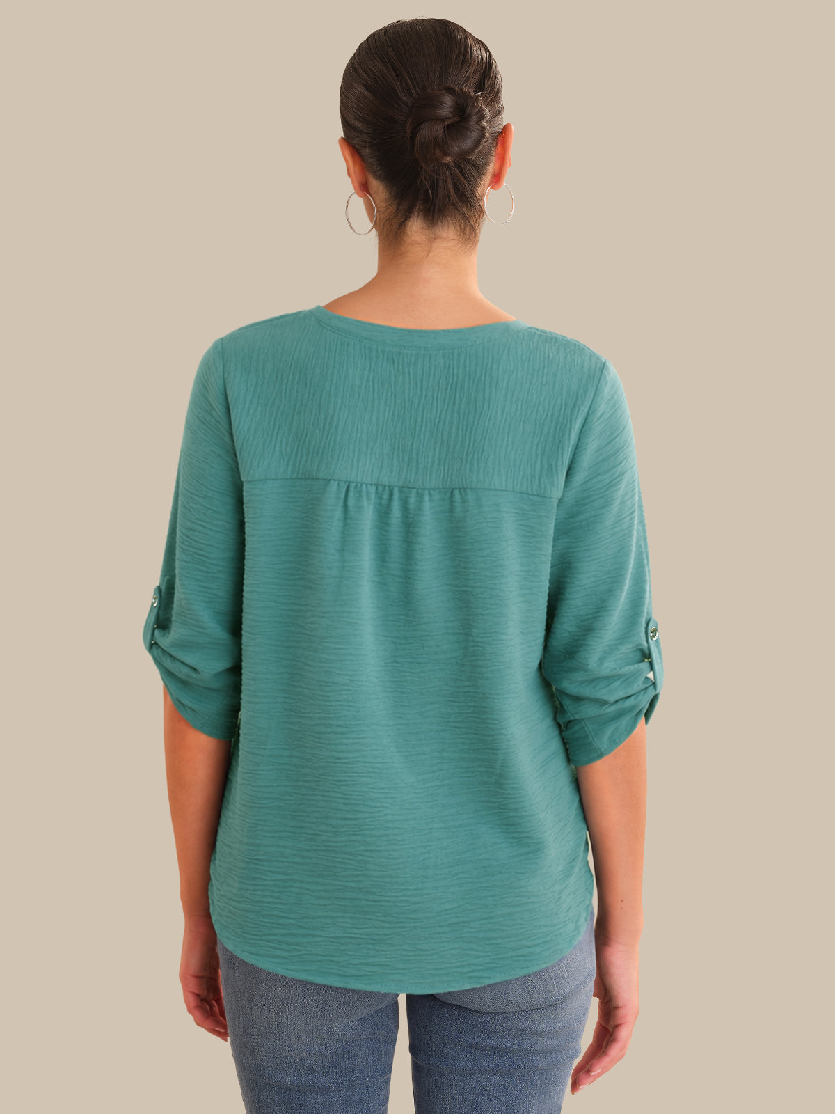 Person wearing a teal long-sleeve top on a beige background