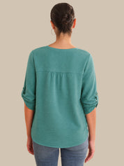 Person wearing a teal long-sleeve top on a beige background