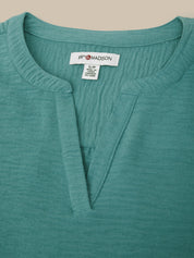 Close-up of a teal shirt with a brand label on a beige background