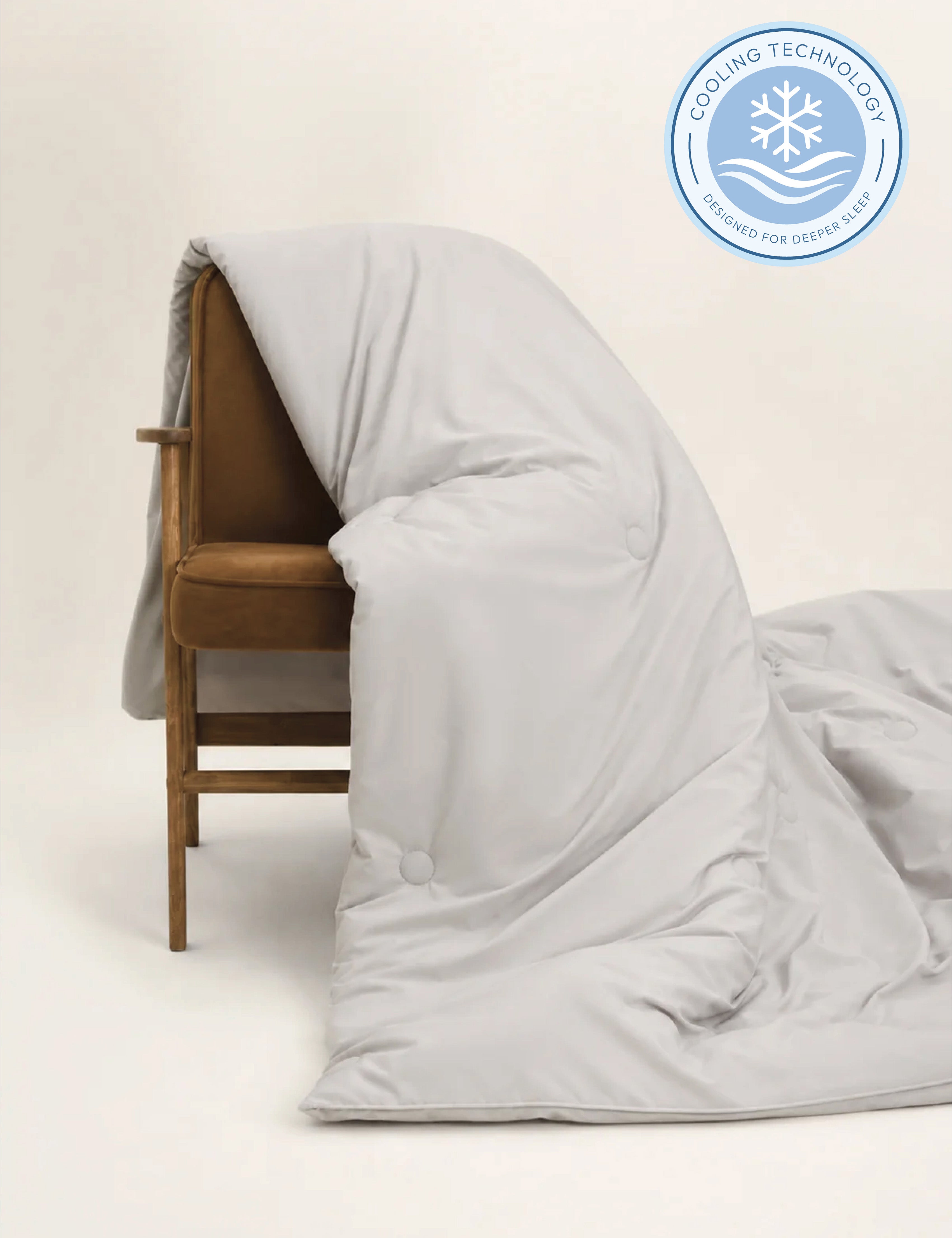 A light gray cooling duvet or comforter draped over a brown upholstered wooden chair, with a circular cooling technology badge in the top right corner.