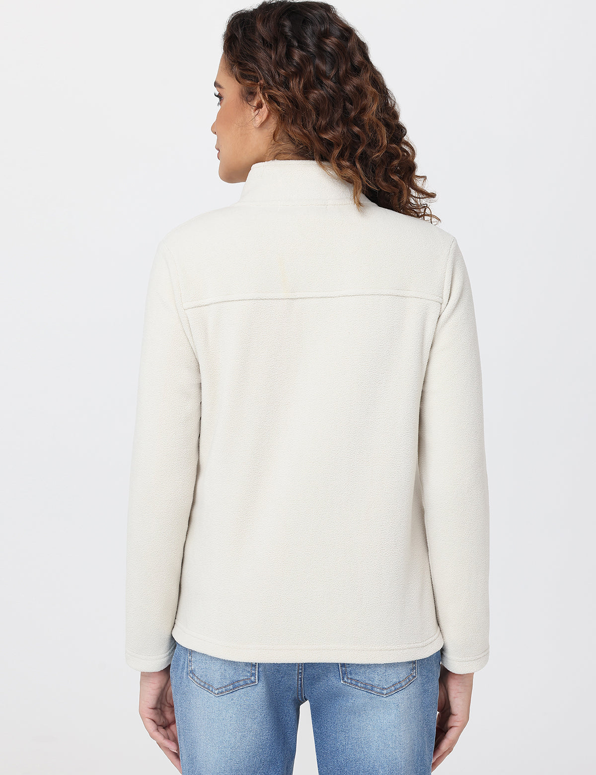 Woman wearing a cream jacket and blue jeans on a white background