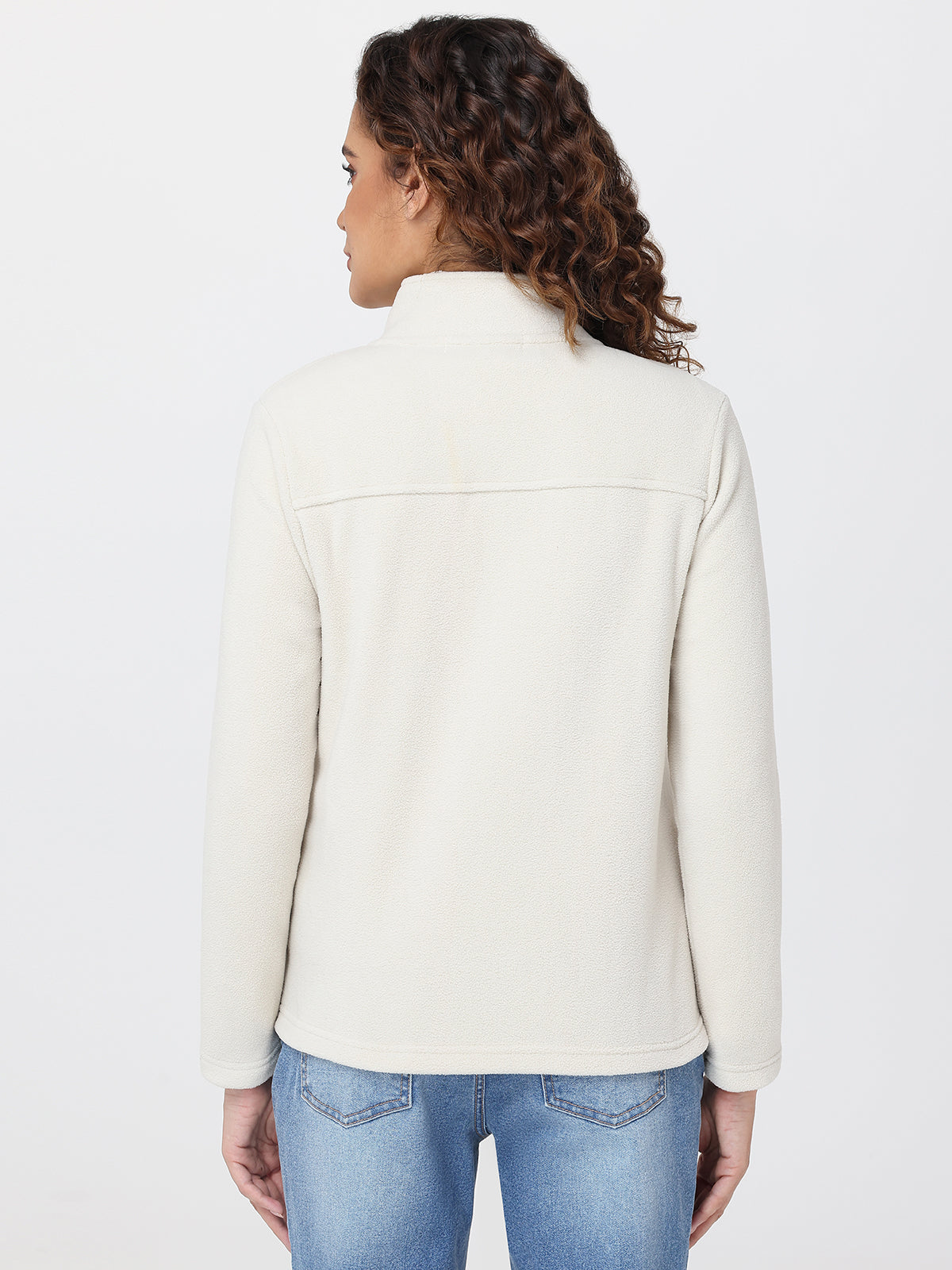 Woman wearing a cream jacket and blue jeans on a white background